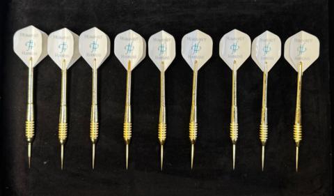 Nine golden darts laid down on a table in a row.