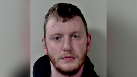 A mugshot of a man with short hair and a beard.