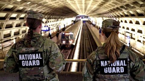 view of the backs of two National Guard members in camo uniforms overlooking a train station in DC