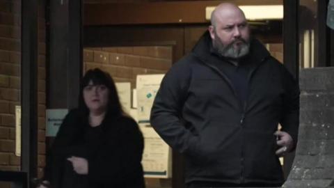 Richard Elkin and Hayley Bell are pictured wearing dark coats outside the main entrance of Portsmouth Crown Court. He is bald with a full, grey beard and she has long, dark hair over her shoulders.