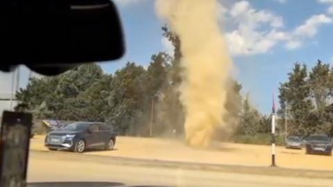 Dust devil swirling around car park between parked cars