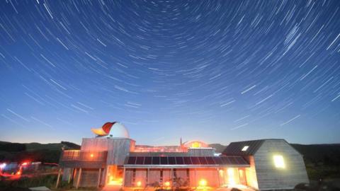 A brightly lit observatory building beneath a swirling starry sky