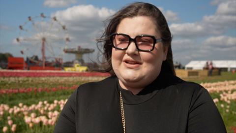 Woman in a black top with glasses and black hair stands in a tulip field.