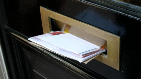 A general view of mail sticking out of the front door letterbox of a residential property.