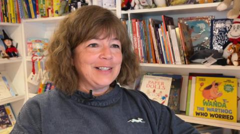 Ginny Sealey smiley at the camera in front of a bookshelf 