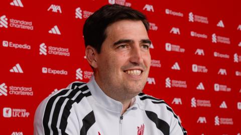 Andoni Iraola sits at the news conference table at Liverpool's training base in Kirkby and smiles.