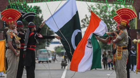 Indian and Pakistani soldiers hold their flags at the India-Pakistan Wagah Post 