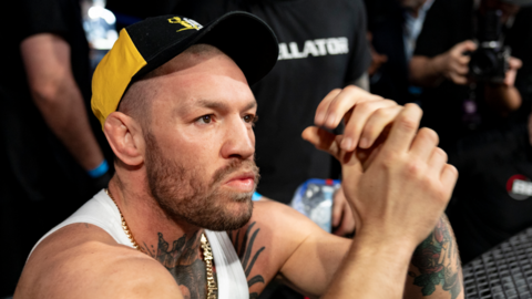 Conor McGregor looks on at cageside in a white top