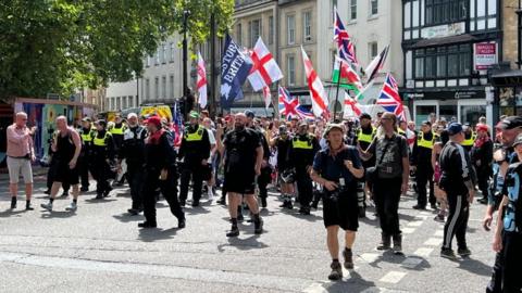 A group of protesters holding English, Welsh and British flags on a street in Bristol city centre along with police.