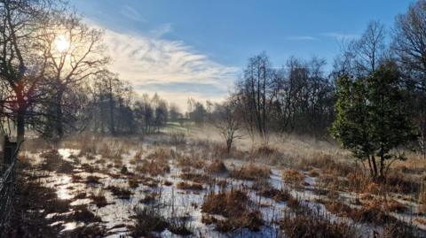 Askham Bog nature reserve photographed on a bright, clear morning. The ground is covered with a mix of patchy snow and frozen puddles, as well as brown grasses and low vegetation.