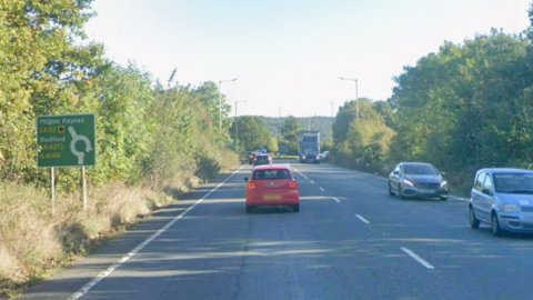 Cars and a lorry travel along the A4146 Fenny Stratford Bypass. It is a sunny day. 