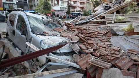 A damaged vehicle lies under the rubble of a collapsed building after an earthquake