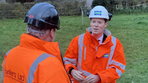 Alex Chalk in an orange hi-vis jacket talking to someone in the same jacket