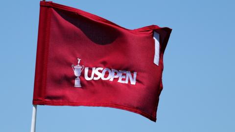 A red flag with an image of the US Open trophy, the words US Open and the number one on it, all in white.