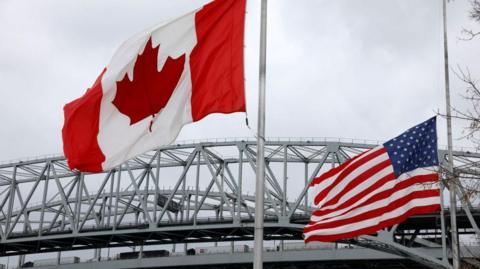 Trucks lined up at the Blue Water Bridge that connects Port Huron, Michigan and Sarnia, Canada in Port Huron, Michigan with the Canada and US flags in the foreground. 