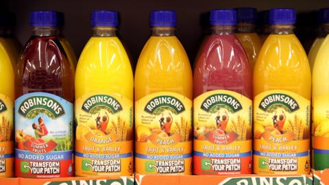 Several bottles of Robinsons squash lined up next to each other on a shelf, in various flavours and colours