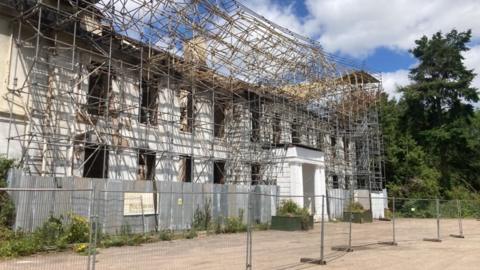 A white house with scaffolding on the outside. It is behind a temporary fence.