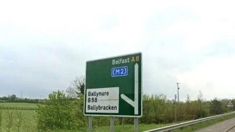A green road sign which shows a left turn leading to Ballynure B58 Ballybracken and straight to Belfast A8. 