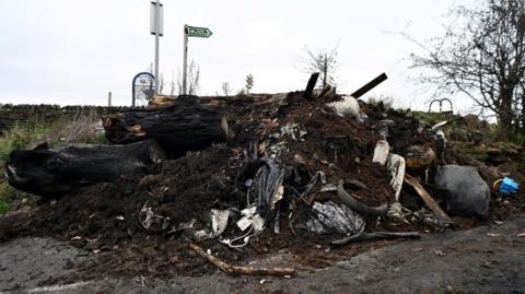 A huge pile of fly-tipped waste, with a load of soil dumped on top.