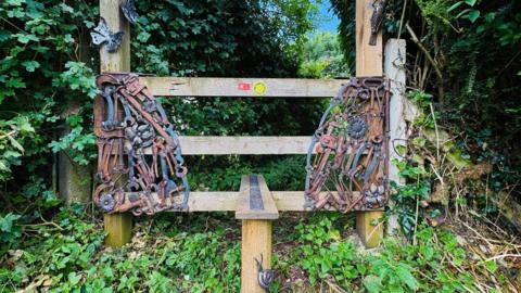 A stile through a hedge with recycled metal tools attached to each side