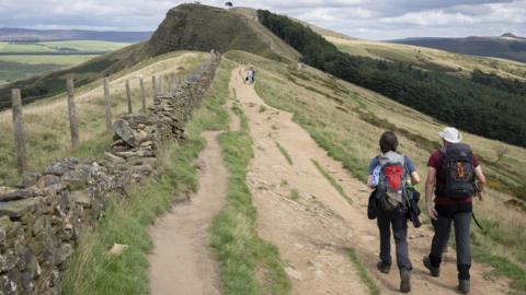 Two walkers wearing rucksacks on a ridge footpath walk in the Peak District