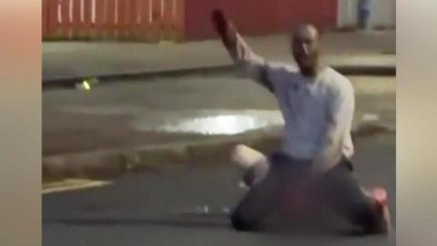 An image from a video circulating on social media. It shows the alleged attacker on top of a man and raising his arm