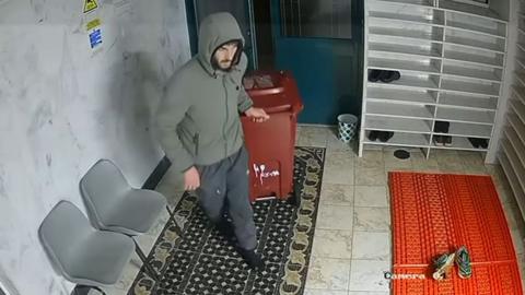 A man with his hood up pulling a burgundy wheelie bin through the mosque entrance