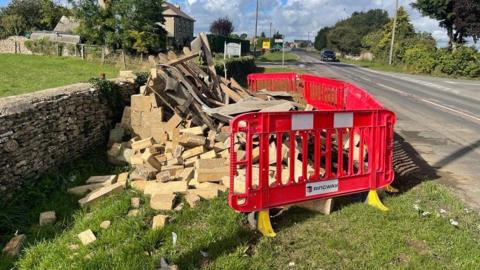 The remains of a stone bus shelter on Cirencester Road, surrounded by red Ringway barriers to keep the public away from the rubble.