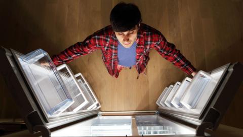 A birds eye view of a man opening a fridge with one door on each hand