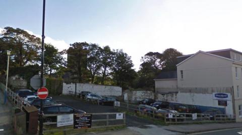 A car park with wooden fencing around it. St George's Church can be seen in the background with trees around it.