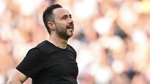 Roberto de Zerbi looking upwards while standing on the touchline