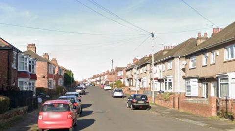 A Google Streetview screenshot of Westminster road. It is a residential street with terraced and semi-detached houses on either side and cars parked on the street.