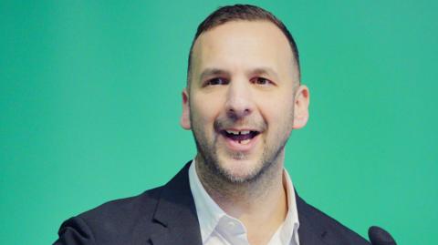 Zack Polanski speaking in front of a Green background