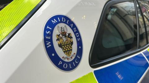 A West Midlands Police emblem on the side of a white and blue police car. 