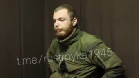 A man believed to be James Scott Rhys Anderson, 22, a former British Army soldier captured while fighting for Ukraine, is seen wearing green military clothing and sat in front of a plain brown background. 