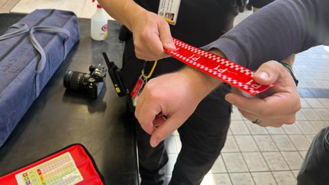 A close-up of a red and white band being put on the wrist of a man by a firefighter.