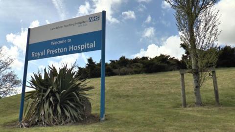 A white sign mounted on a grassy hill reads: Welcome to Royal Preston Hospital. 