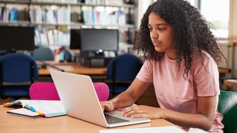 GCSE maths image: A student works on a laptop in a library revising maths.