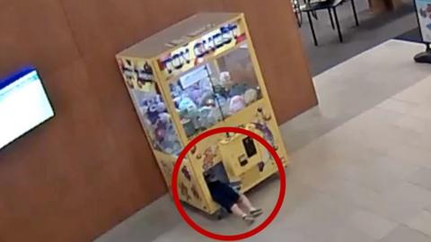 Child is climbing inside a claw machine.