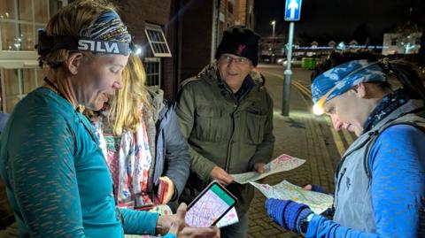 Two women in headtorches study maps beside a darkened street.