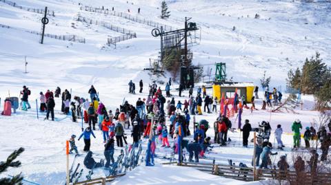 Crowds of snowsports enthusiasts in colourful ski wear at Cairngorm Mountain. It is a bright, sunny day.