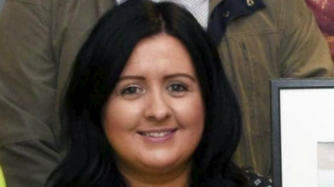 A woman is seen with long black hair and is smiling. 
A number of people are seen near here, but their faces are not visible.
