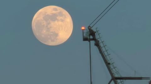 photo of the full moon on Tuesday morning rising next to a crane
