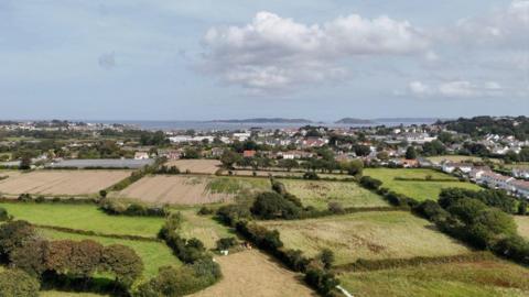 Drone shot overlooking part of Guernsey with fields in the foreground. The islands of Herm, Jethou and Sark are in the background.