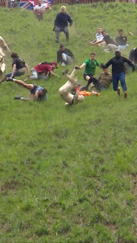 People rolling down a hill chasing a cheese.