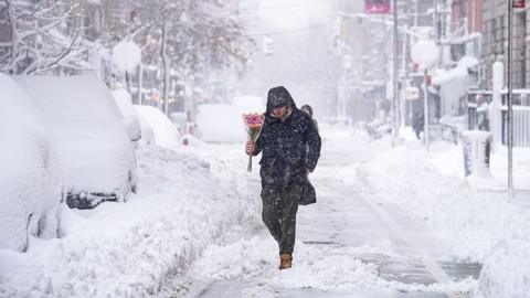 A person walks through a snow filled street carrying a bundle of pink flowers