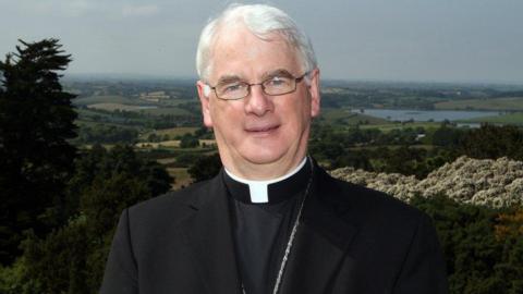 Noel Trainor, grey hair wearing glasses, with countryside behind him