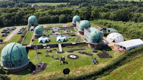 A drone image of the Observatory Science Centre at Herstmonceux, showing six green copper domes, with smaller buildings dotted between them.