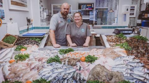 Man and woman in fishmongers with display of fish