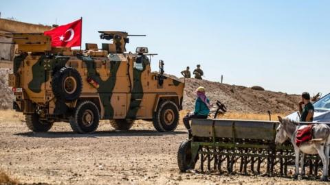 Turkish military vehicles drive on a patrol in the Syrian village of al-Hashisha on the outskirts of Tal Abyad